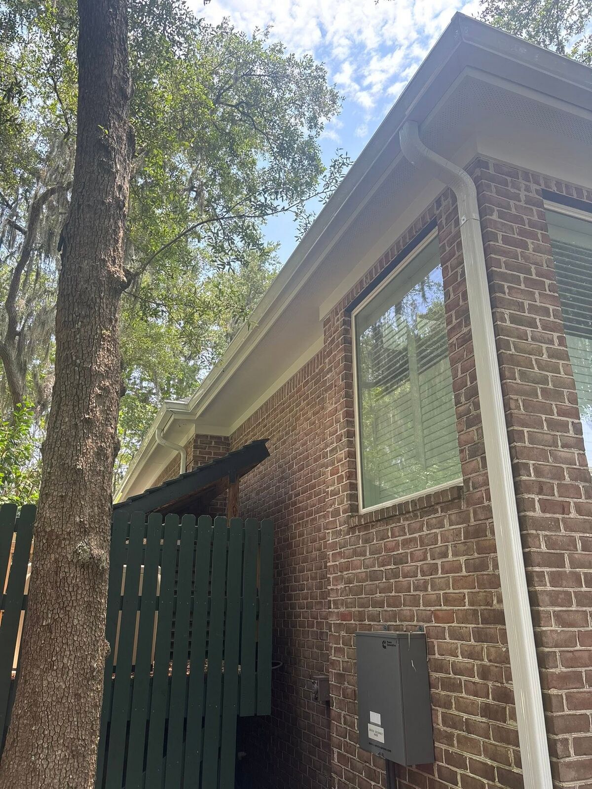 White seamless downspout routed cleanly down a brick column on a Lowcountry home
