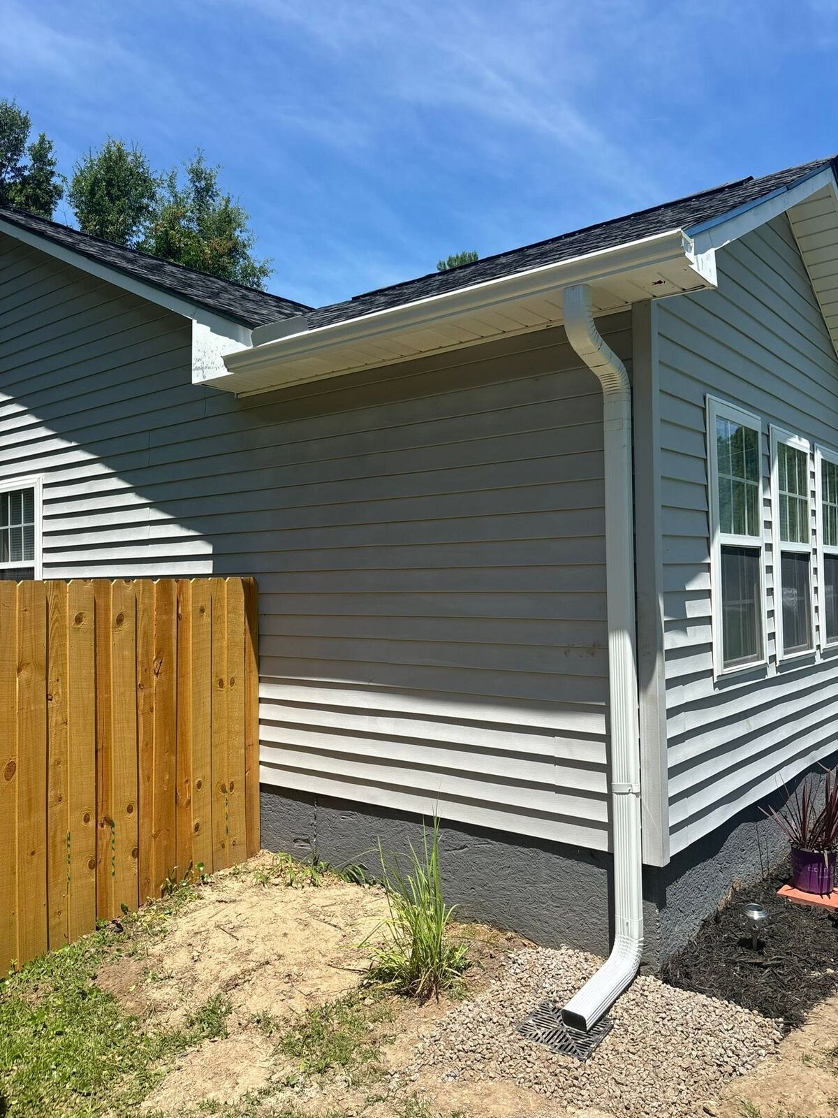 White gutter and downspout on a gray clapboard home with a rain splash block