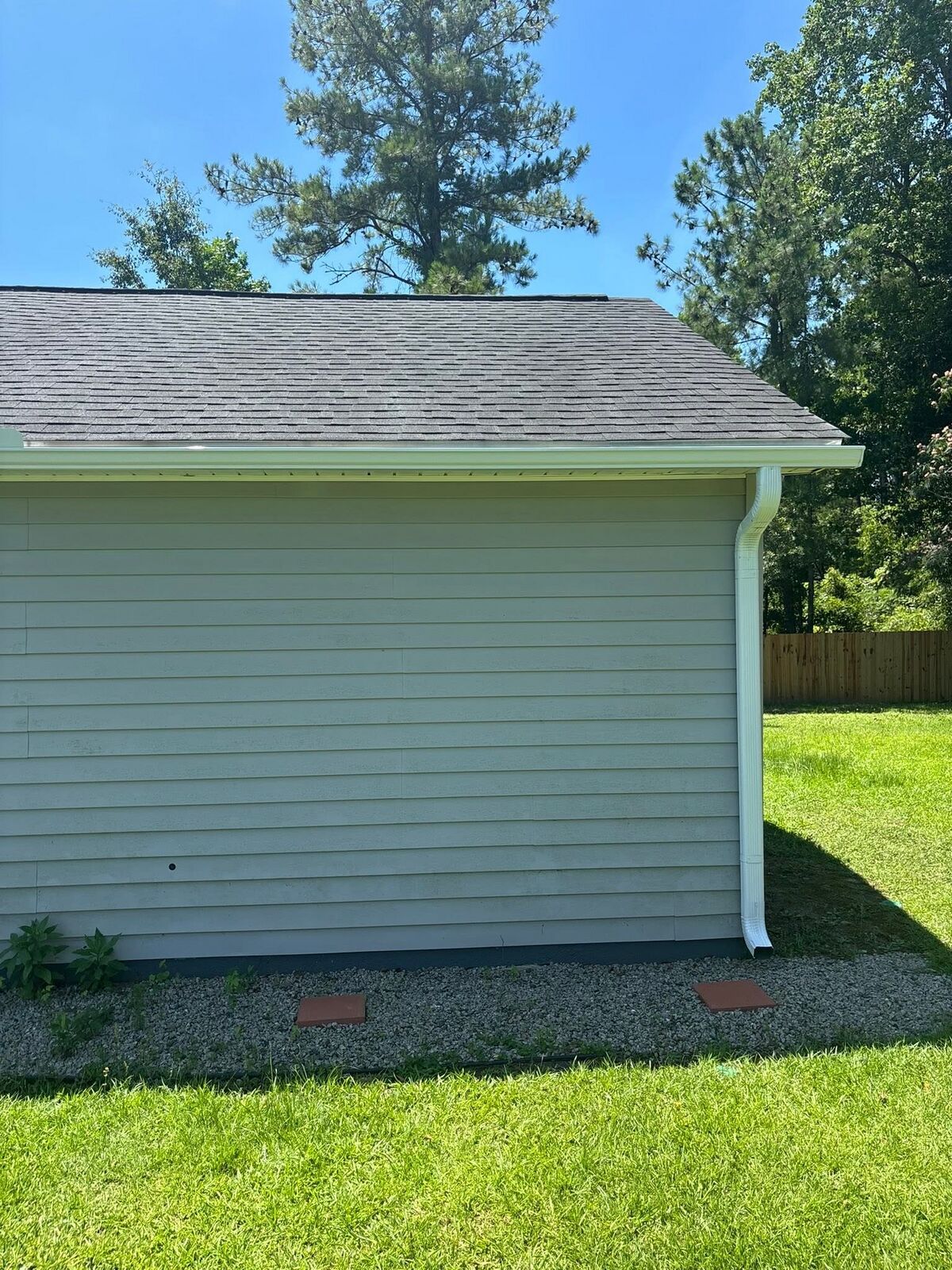 Seamless gutter and downspout draining to gravel on a light-green home